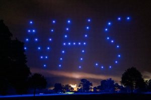 Image of a drone light show, with the drones forming the letters NHS