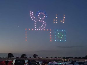 A colorful drone light display at dusk forms a DJ playing music above a crowd, turning the event into an unforgettable drone show.