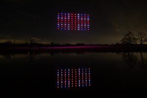 The drone light show dazzles as drones display "2023" in red and blue lights in the night sky, their vibrant colors reflecting beautifully in the body of water below.