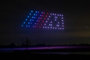 A dark night sky features an illuminated rectangular shape, formed brilliantly by a drone light show in blue, red, and white lights.