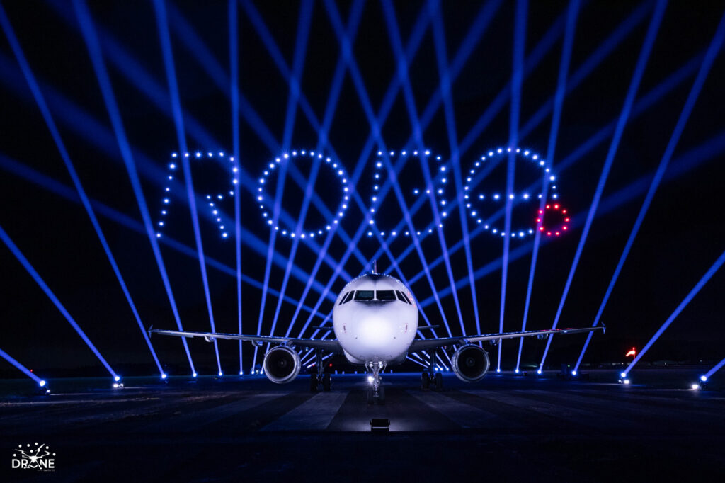 An airplane on a runway at night with “ROUTE” spelled in lights and blue beams in the background.