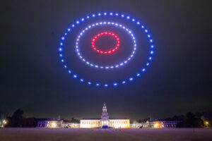 Drones form red and blue concentric circles in the night sky above a large, illuminated building.