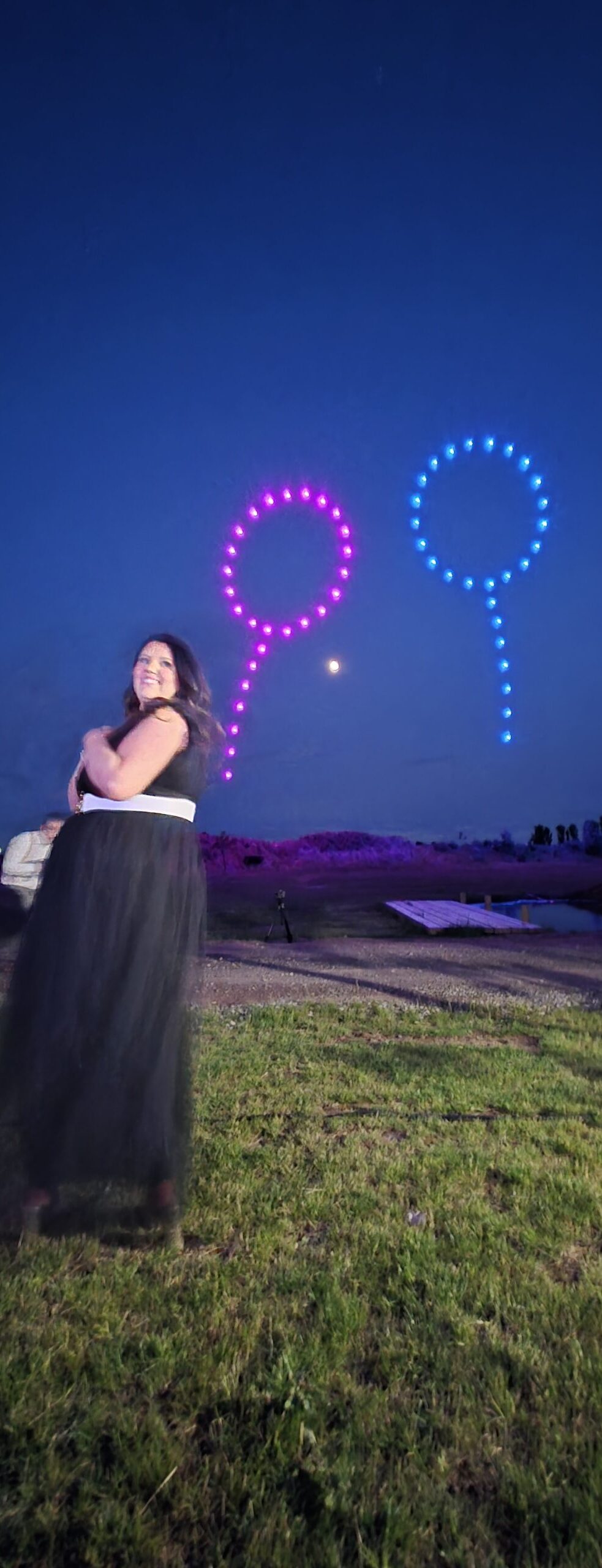 Woman in a black dress stands outdoors at night, with colorful drone light balloons illuminating the sky behind her—sorry, there are no important SEO keywords in the description.